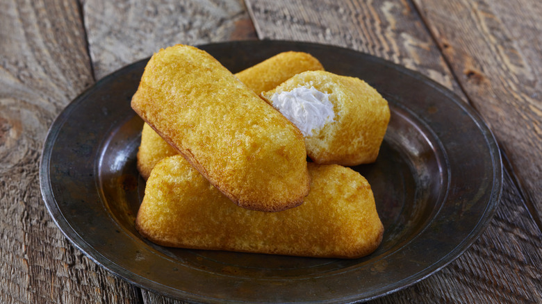 Several hostess twinkies piled on a black plate.