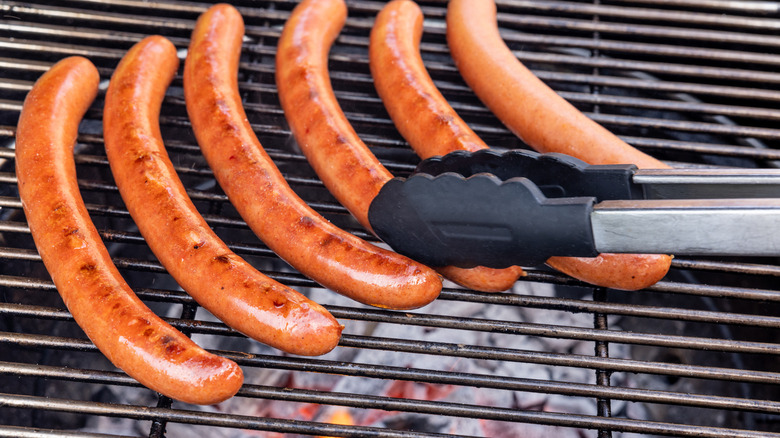 Hot dogs over charcoal grill being flipped with tongs.