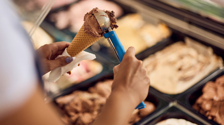 A person scooping chocolate ice cream into a cone