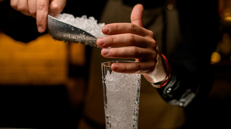 Bartender scoops ice into a glass with ice scoop.