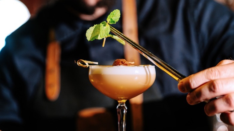 Bartender uses tongs to add garnish to a cocktail.