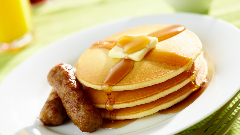 White plate with stack of pancakes with butter and syrup and sausage links