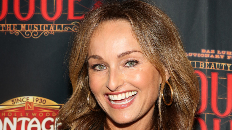 Headshot of Giada De Laurentiis tilting head and smiling in front of marketed background