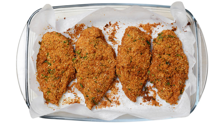 Glass baking dish with parchment and 4 pieces of browned crispy chicken breasts