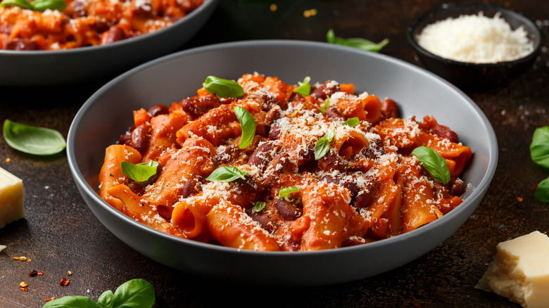 A grey bowl of pasta e fagioli garnished with basil leaves and grated parmesan cheese