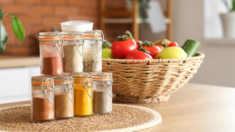 Spice jars stacked on counter next to bowl of fresh vegetables on kitchen counter