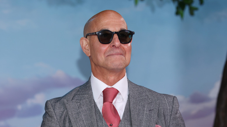 Stanley Tucci smiling at the camera wearing a suit and sunglasses.