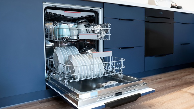 Open dishwasher with dishes inside and blue kitchen cabinets
