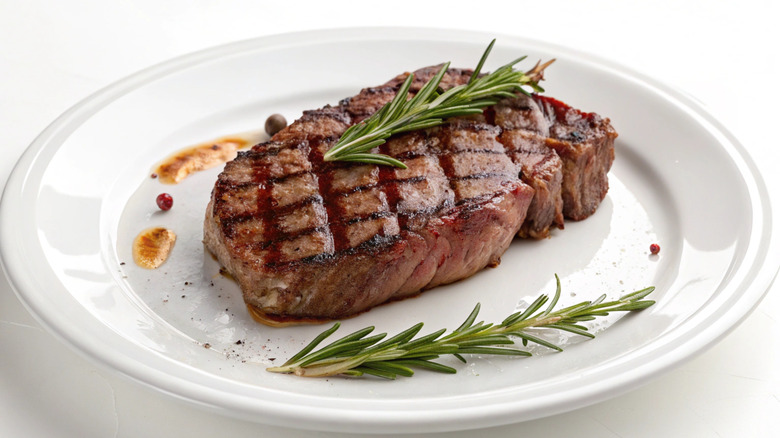 Ribeye steak with grill marks and rosemary sprigs on white plate