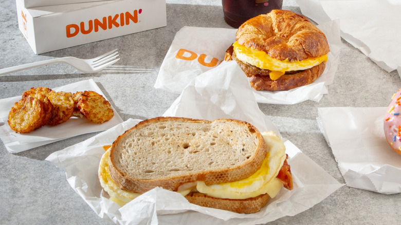A Dunkin' sourdough breakfast sandwich with hash browns, a croissant sandwich, and a drink