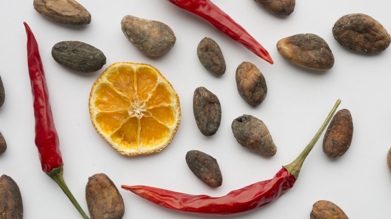 Dried cacao beans, chiles, and citrus on a white surface