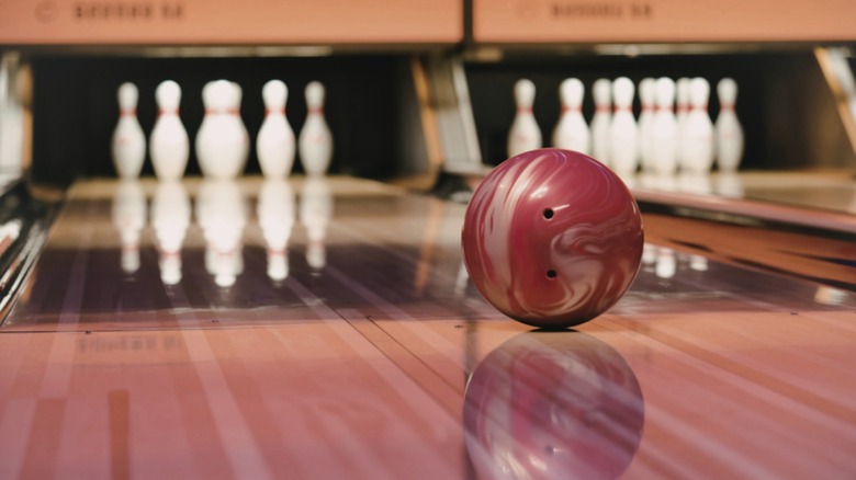 A red bowling ball rolling down a wood lane toward white pins