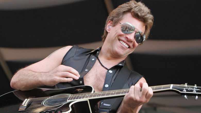 Jon Bon Jovi playing guitar with aviator sunglasses on at a concert