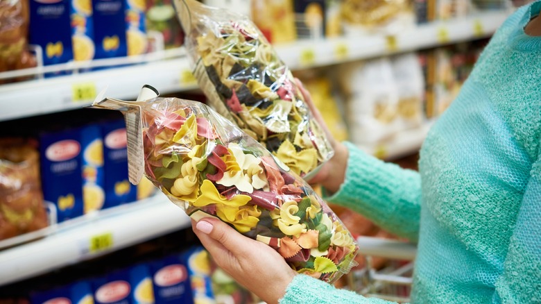 Person looking at two types of pasta in plastic bags in store