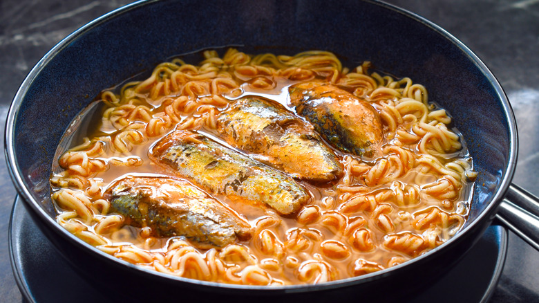 A blue bowl of tomato-based ramen with seafood in it