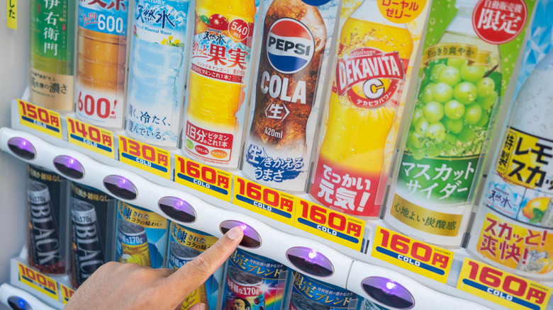 A finger pressing the Pepsi Cola button on a Japanese vending machine.