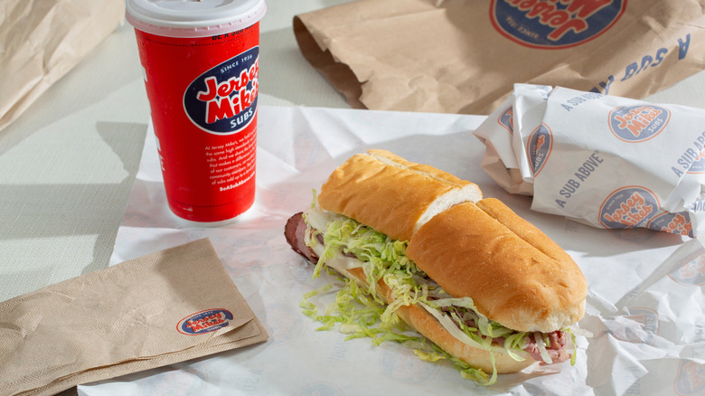 A Jersey Mike's sub sandwich with a drink on sandwich paper.