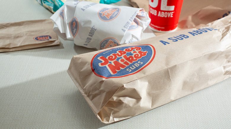 A wrapped Jersey Mike's sub sandwich with a drink on a table.