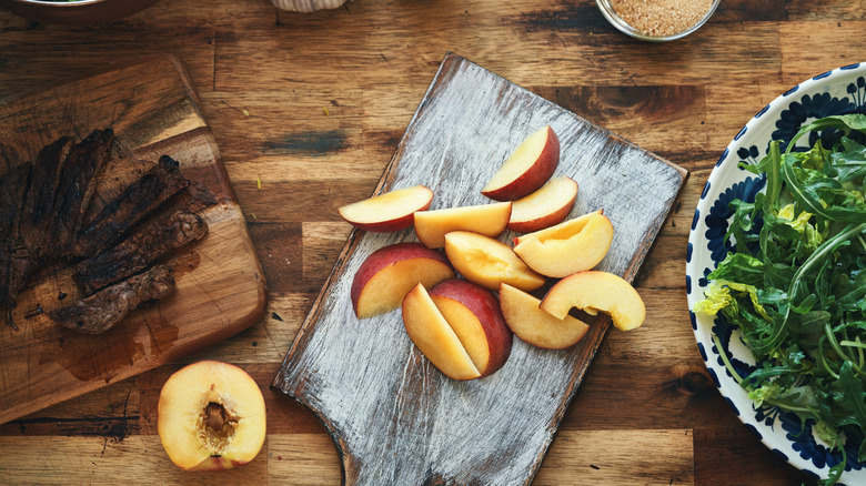 Steak and peaches laid out on a counter near a bowl of greens
