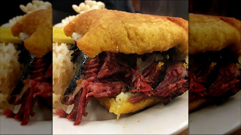 A pastrami on a knish sandwich with mustard and sauerkraut on it.