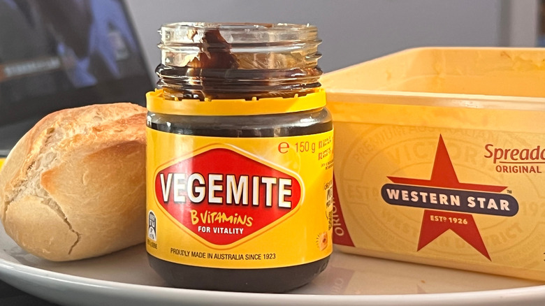 An open jar of Vegemite pictured with Western Star butter spread and a bread roll