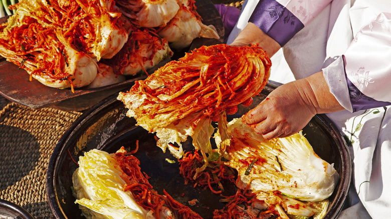 A cook prepares kimchi in a large metal basin