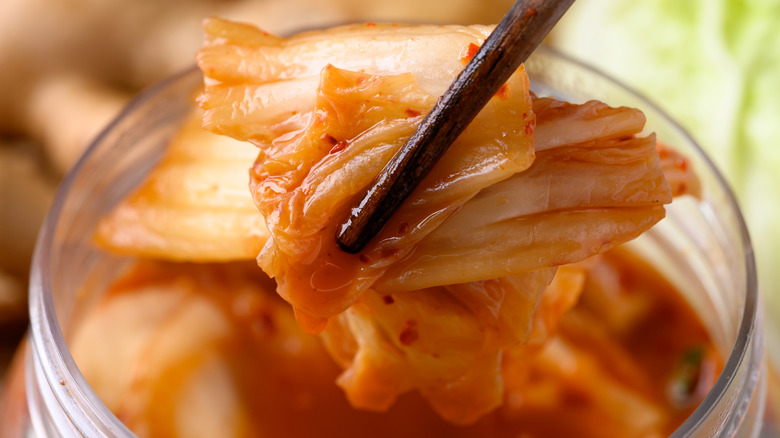 A pair of chopsticks hold kimchi above a jar