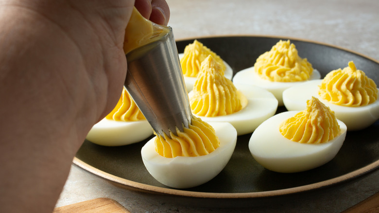 A hand piping filling into deviled eggs
