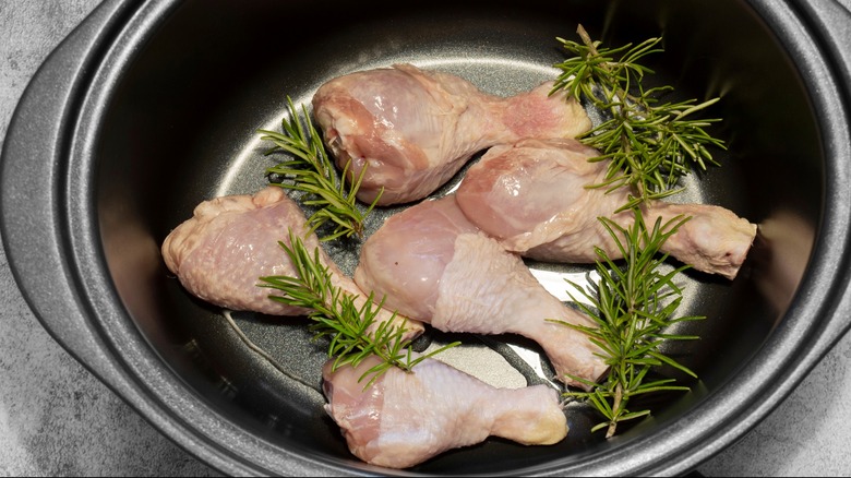 Raw chicken drumsticks with rosemary in a slow cooker