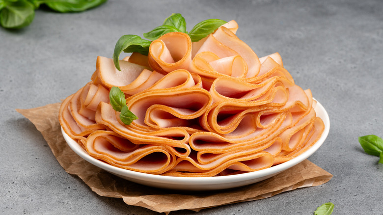 A plate of sliced turkey deli meat, garnished with basil