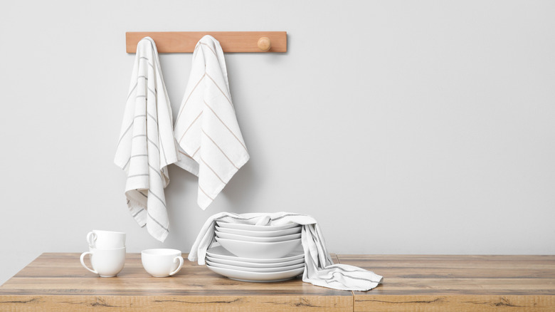 Clean towels hanging on the wall and dishes and cups placed on a wooden counter in the kitchen.
