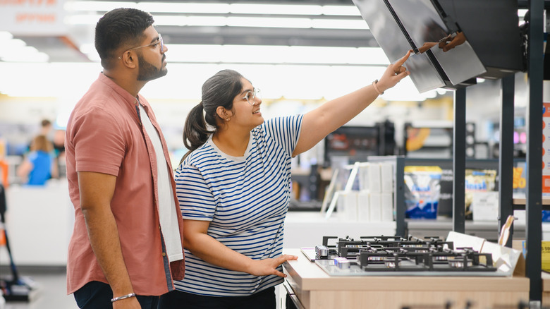 Two people look at a signage above a stove top range at an applicance store