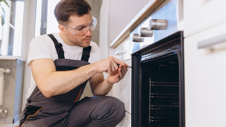 A man in overalls and safety goggles repairs an oven.