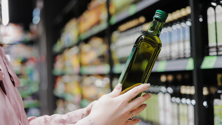 Female hands holding a bottle of natural olive oil at the grocery store.