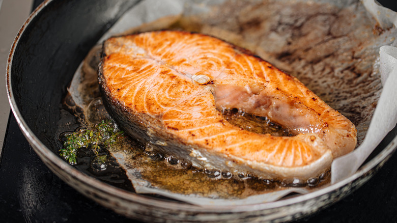 Salmon cooks with oil and herbs on top of parchment paper in a pan
