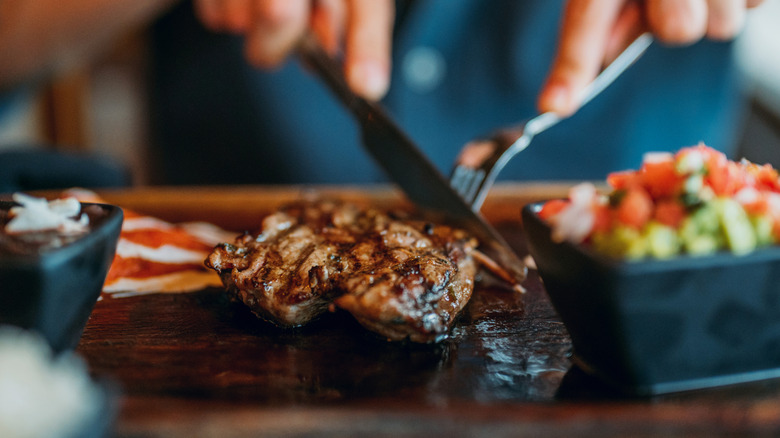 Cutting a piece of steak on a wooden serving board