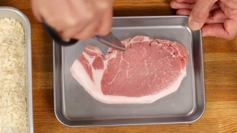 Person making cuts in a pork chop with scissors.