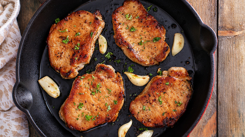 Four pork chops in a skillet with garlic.
