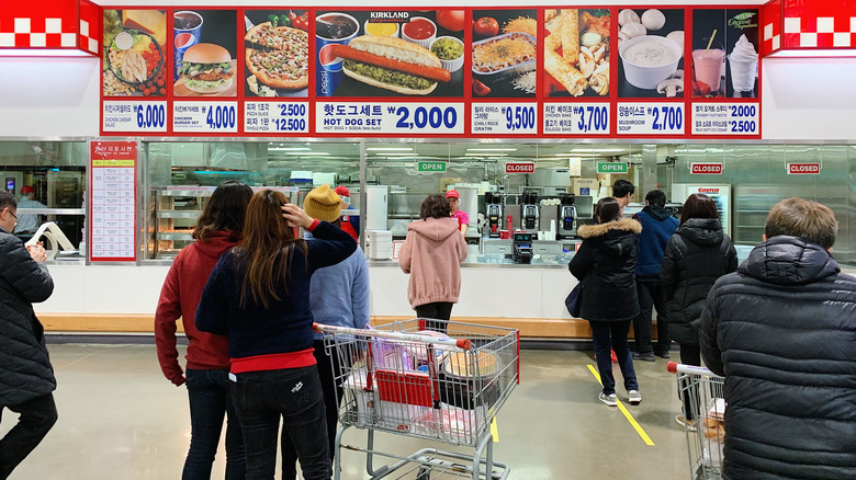 Food court at a Korean Costco with a menu board with photos and people in front of it