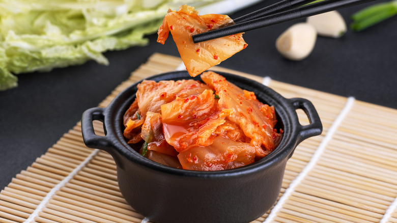 Chopsticks picking up a piece of kimchi from a black crock