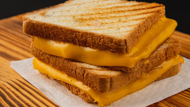 A closeup of two grilled cheese sandwiches on white paper, stacked