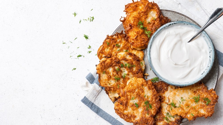 Potato latkes plated with bowl of herbs and sour cream with utensil