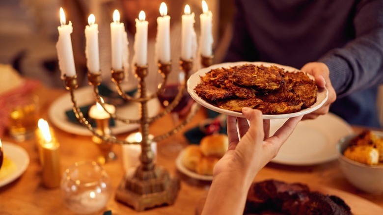 Two people passing latkes to each other across a table at Hanukkah