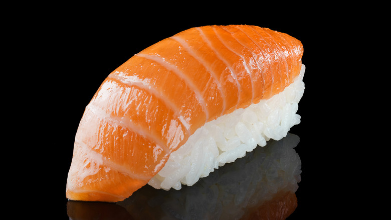 A piece of salmon nigiri on an all-black reflective background