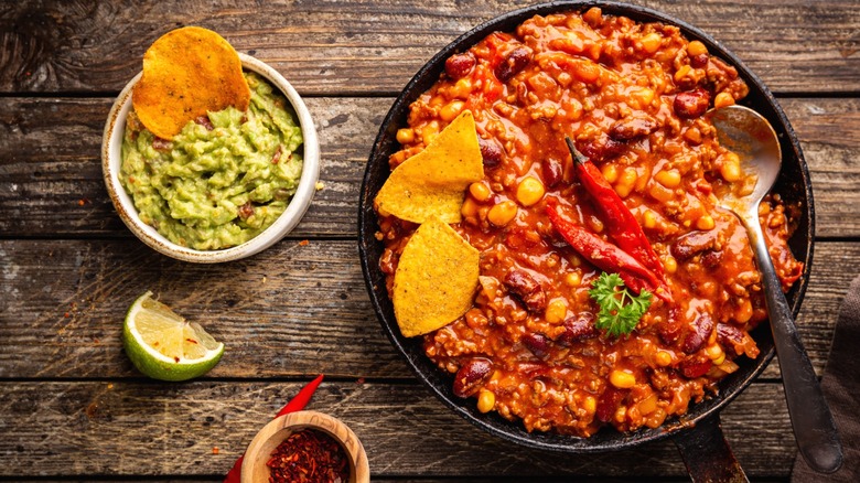 A bowl of chili with guacamole and tortilla chips.