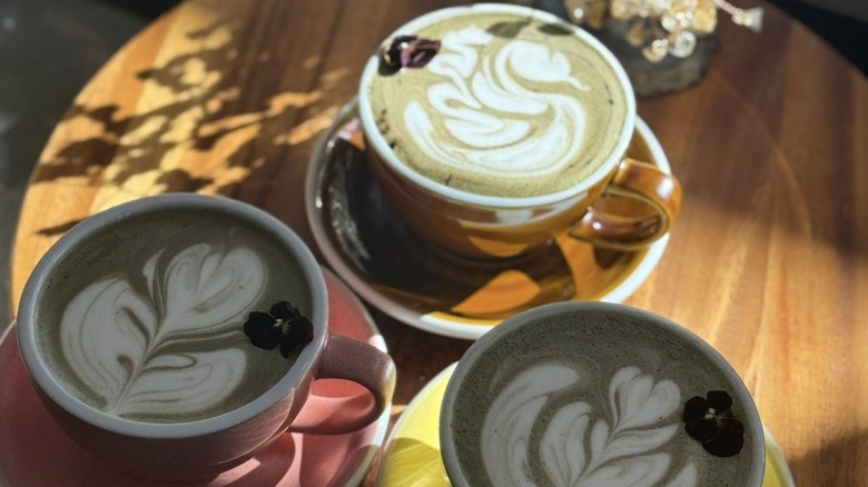 Three coffee drinks with latte art from Coffeegraph on a wooden table with sunshine streaming in
