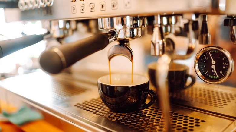 Espresso is poured from espresso machine into a black cup. Small business, beverage concept