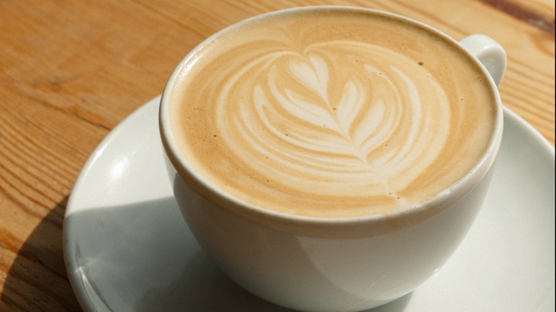 Latte with latte art in white cup on saucer on wood table from Thunder Coffee