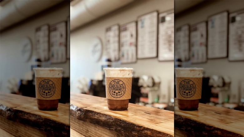 Iced coffee drink in to-go cup with logo sleeve on it sitting on wooden counter at Chocolate Moose Coffee