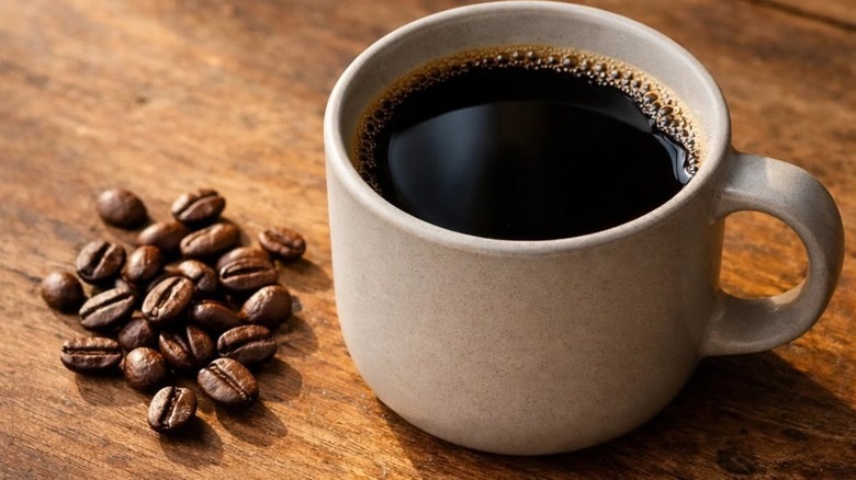 Cup of coffee on wooden table with a few coffee beans scattered on the side at Rasta Barista